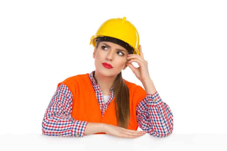 Young woman in yellow hardhat, orange reflective vest and lumberjack shirt leans on a white banner, scrathing head, looking up and thinking. Studio shot isolated on white. thinking over naming strategy pic for Sue-Ann Bubacz post on WriteMixforBusiness